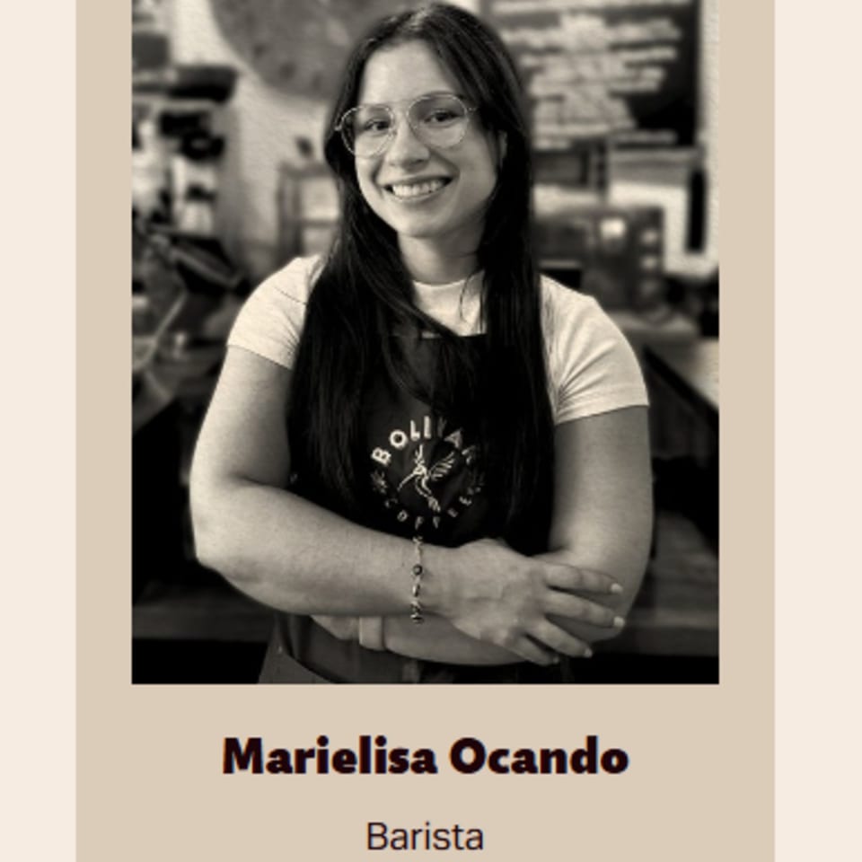 Smiling barista Marielisa Ocando wearing glasses and a Bolivar Coffee apron, arms crossed.