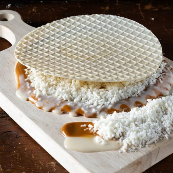 A large, round waffle cookie with dulce de leche and shredded coconut on a wooden board.