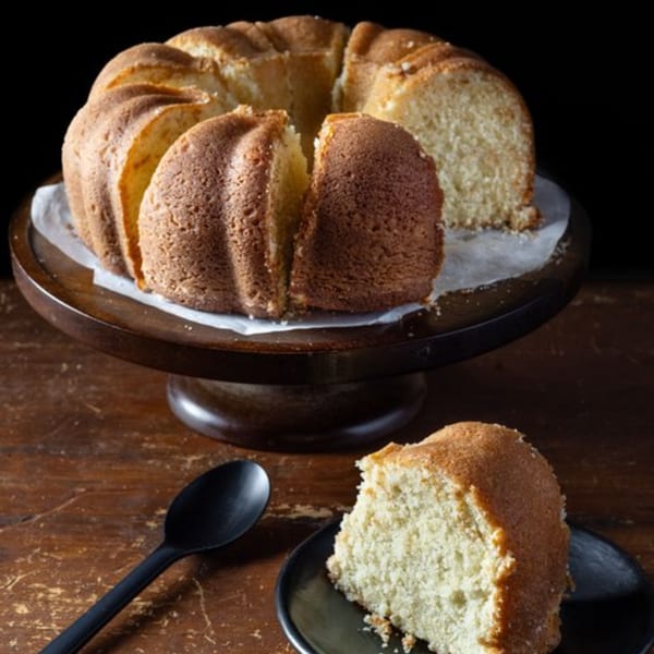 A sliced bundt cake on a wooden stand, with a slice on a plate and a spoon.