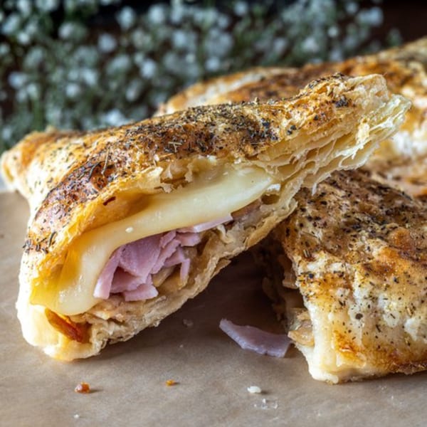 Close-up of a golden-brown pastry, cut open to reveal layers of ham and melted cheese.