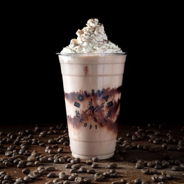 Bolivar Coffee's mocha frappe with whipped cream and chocolate drizzle, surrounded by coffee beans.