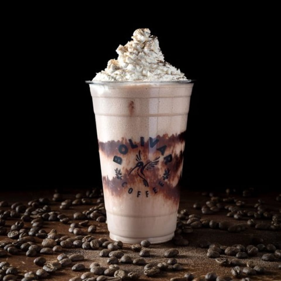 Bolivar Coffee's mocha frappe with whipped cream and chocolate drizzle, surrounded by coffee beans.