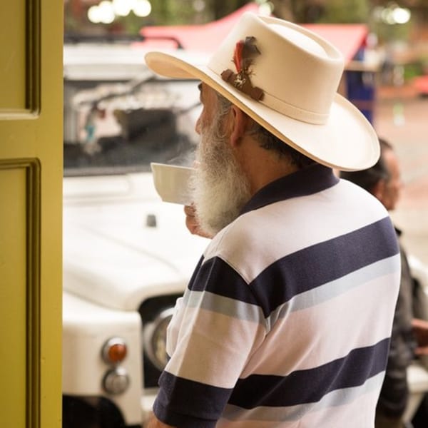 A man with a white beard and cowboy hat sips coffee, looking out from Bolivar Coffee.