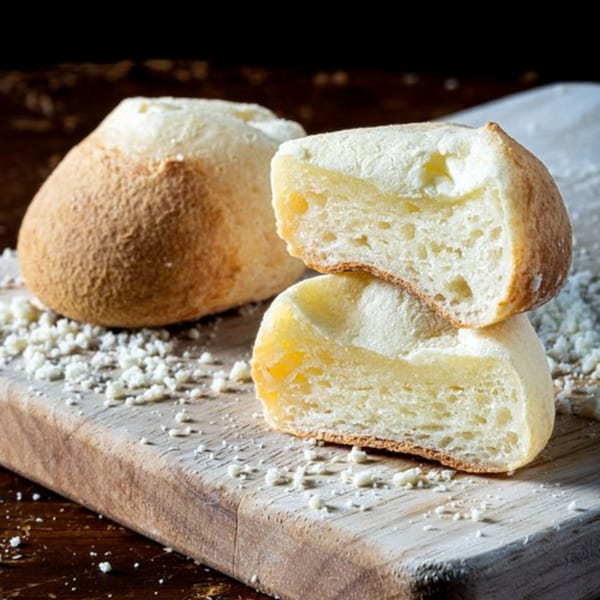 Two Bolivar Coffee cheese breads on a wooden board, one whole and one sliced, with cheese crumbs.