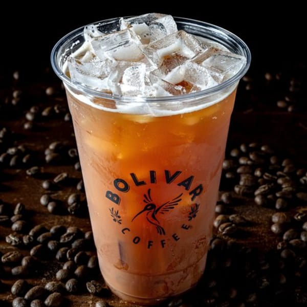 Iced coffee in a clear Bolivar Coffee cup, surrounded by scattered coffee beans.