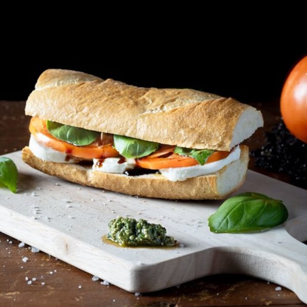 Caprese baguette sandwich with mozzarella, tomato, basil, and balsamic glaze on a cutting board.